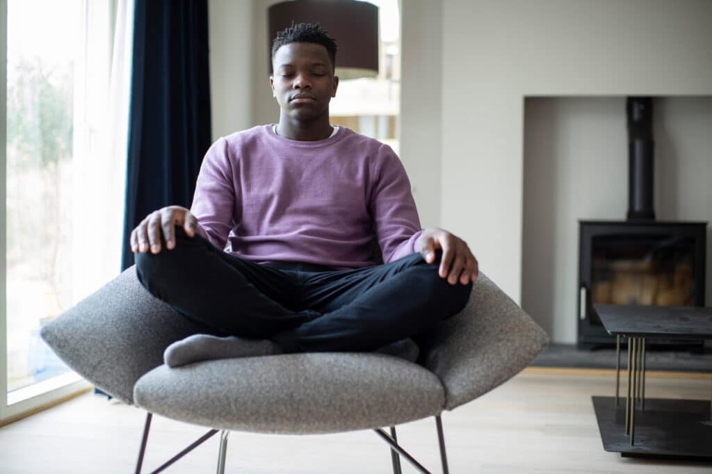 Close Up Of Peaceful Teenage Boy Meditating Sitting In Chair At