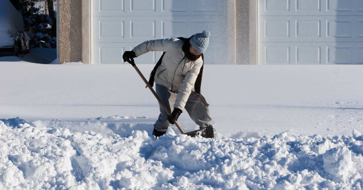 Adult in winter clothing walking outdoors or standing near a sidewalk, shoveling snow with bad posture and hurting spine.