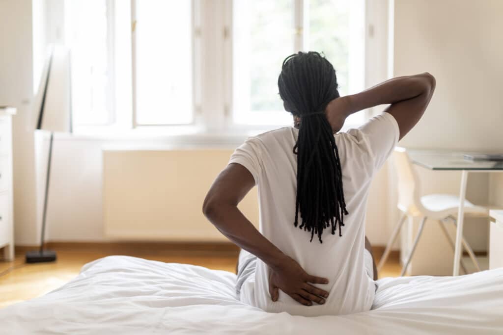 Woman sitting on bed with lower back discomfort from back pain that comes and goes